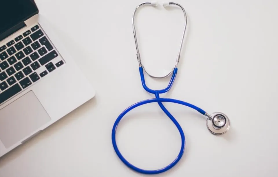 A stethoscope and laptop on a clean white desk.